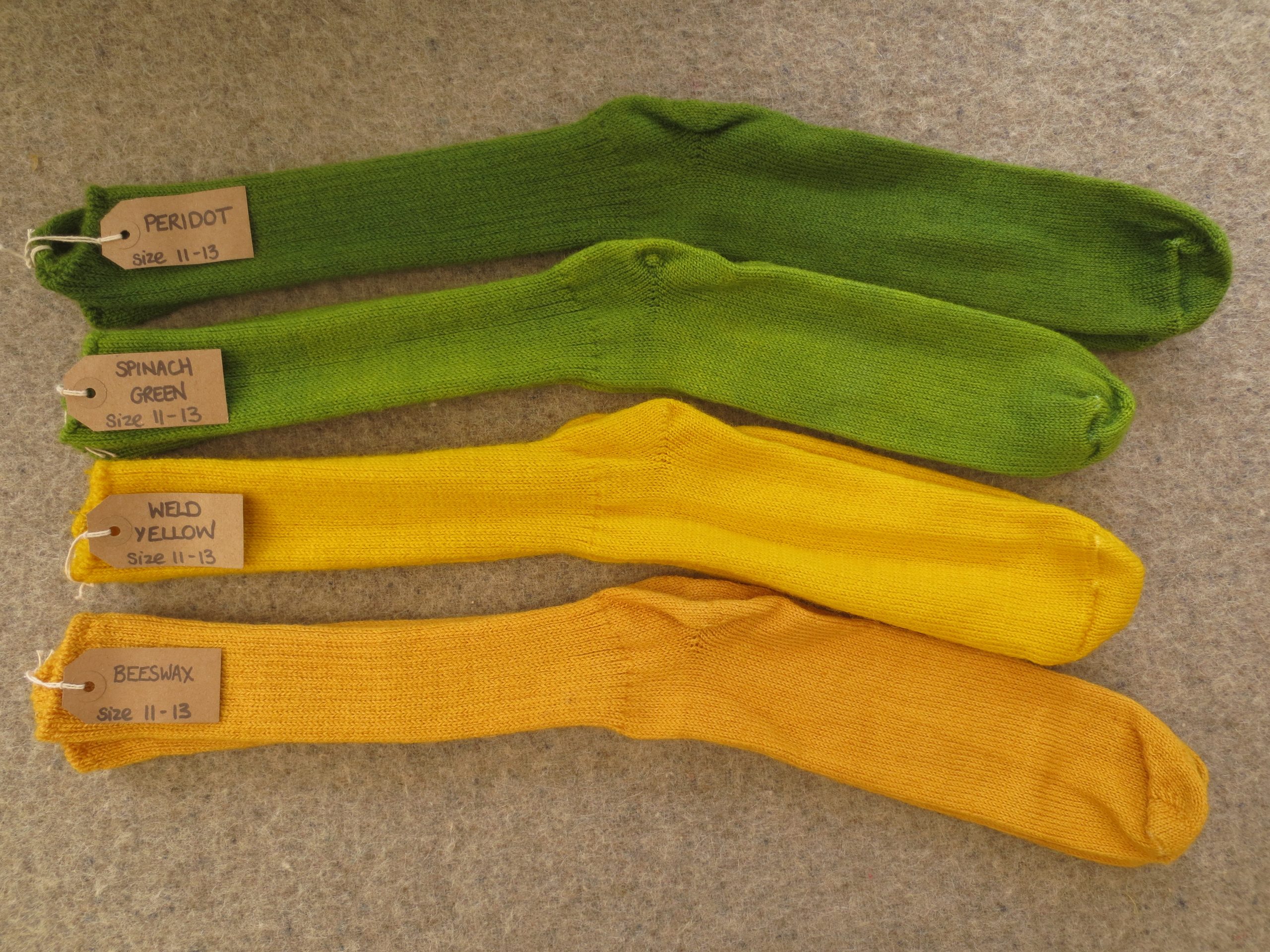 4 pairs of socks labelled Peridot, Spinach Green, Weld Yellow and Beeswax
