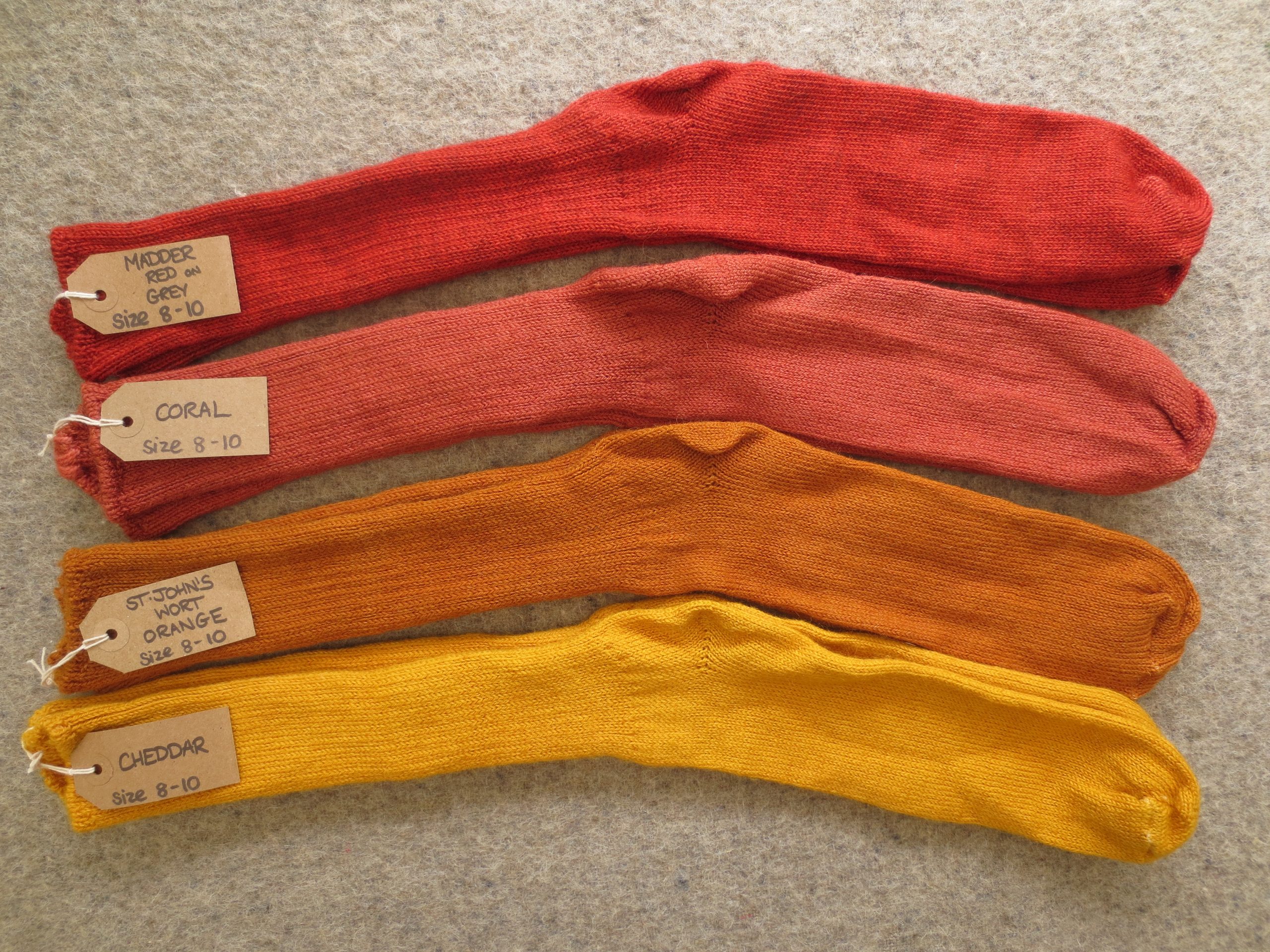 4 pairs of socks labelled Madder Red on Grey, Coral, St John's Wort Orange and Cheddar