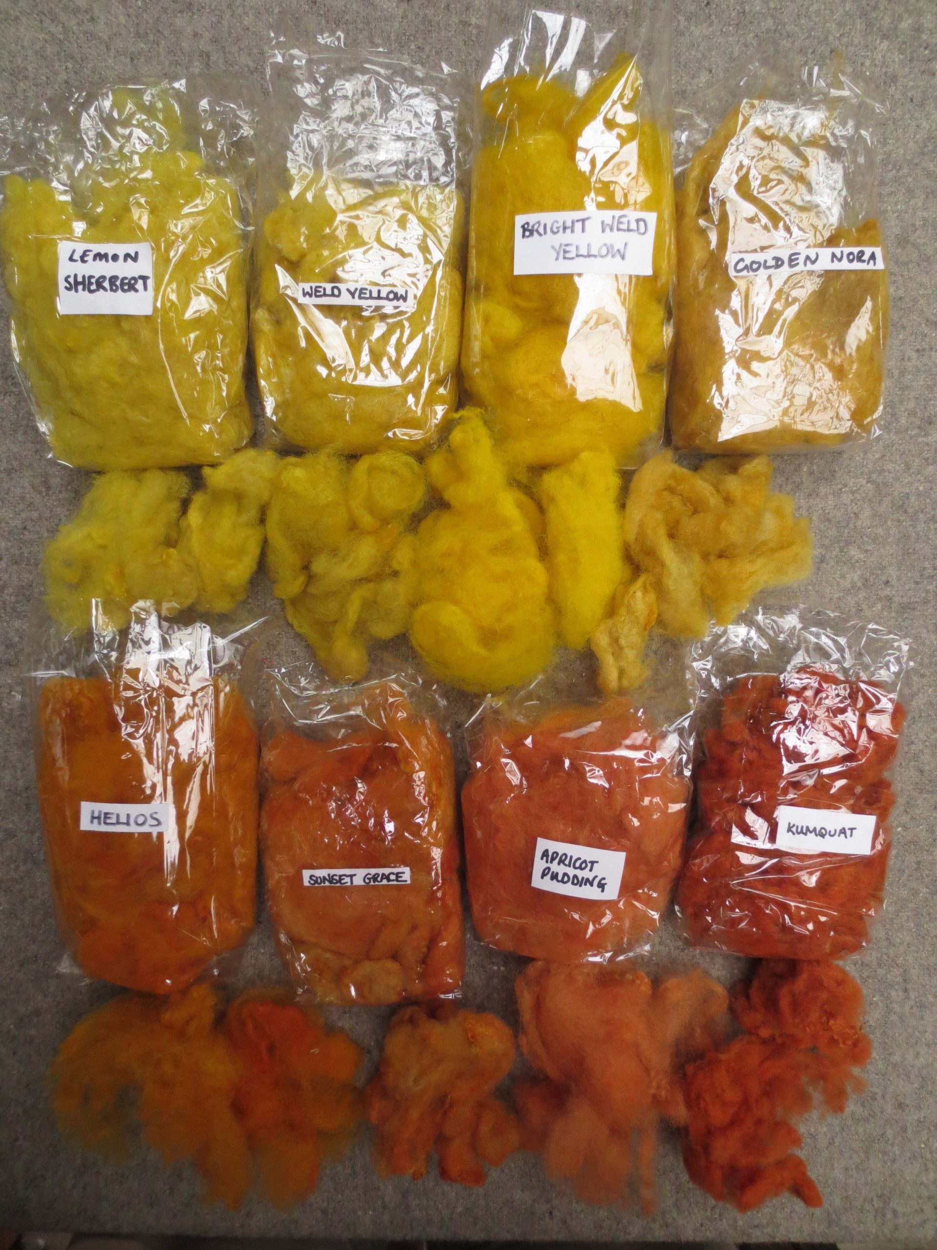 8 bags of labelled wool with examples out of bag labelled lemon sherbert, weld yellow, bright weld yellow, golden Nora, Helios, Sunset Grace, Apricot Pudding and Kumquat